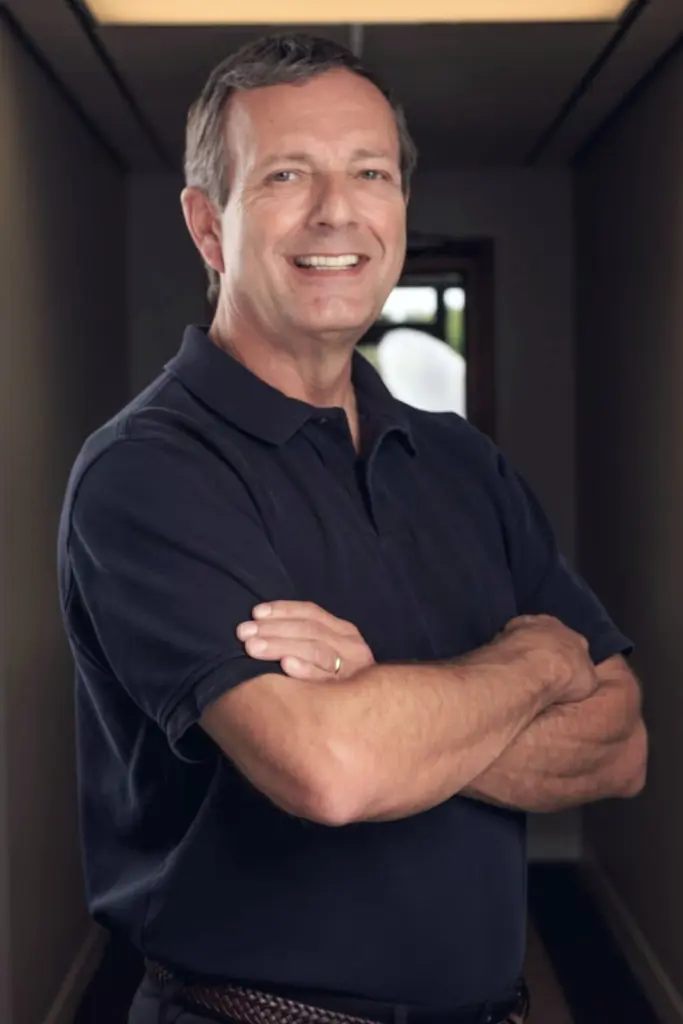 Chuck Renner, OTR, CHT, smiling with his arms crossed, in a dark polo shirt